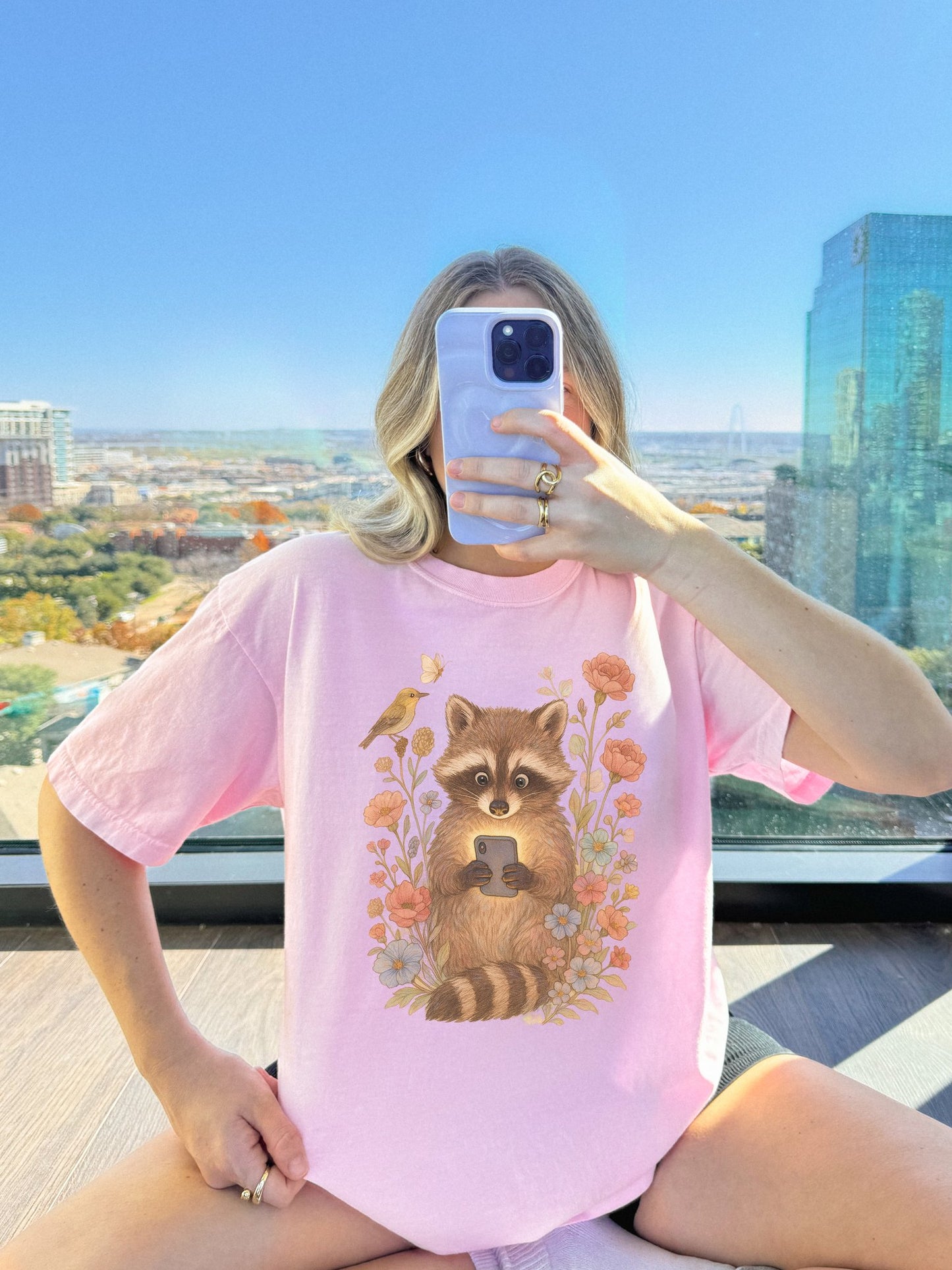 T-shirt with cute raccoon holding smartphone surrounded by coral and blue wildflowers