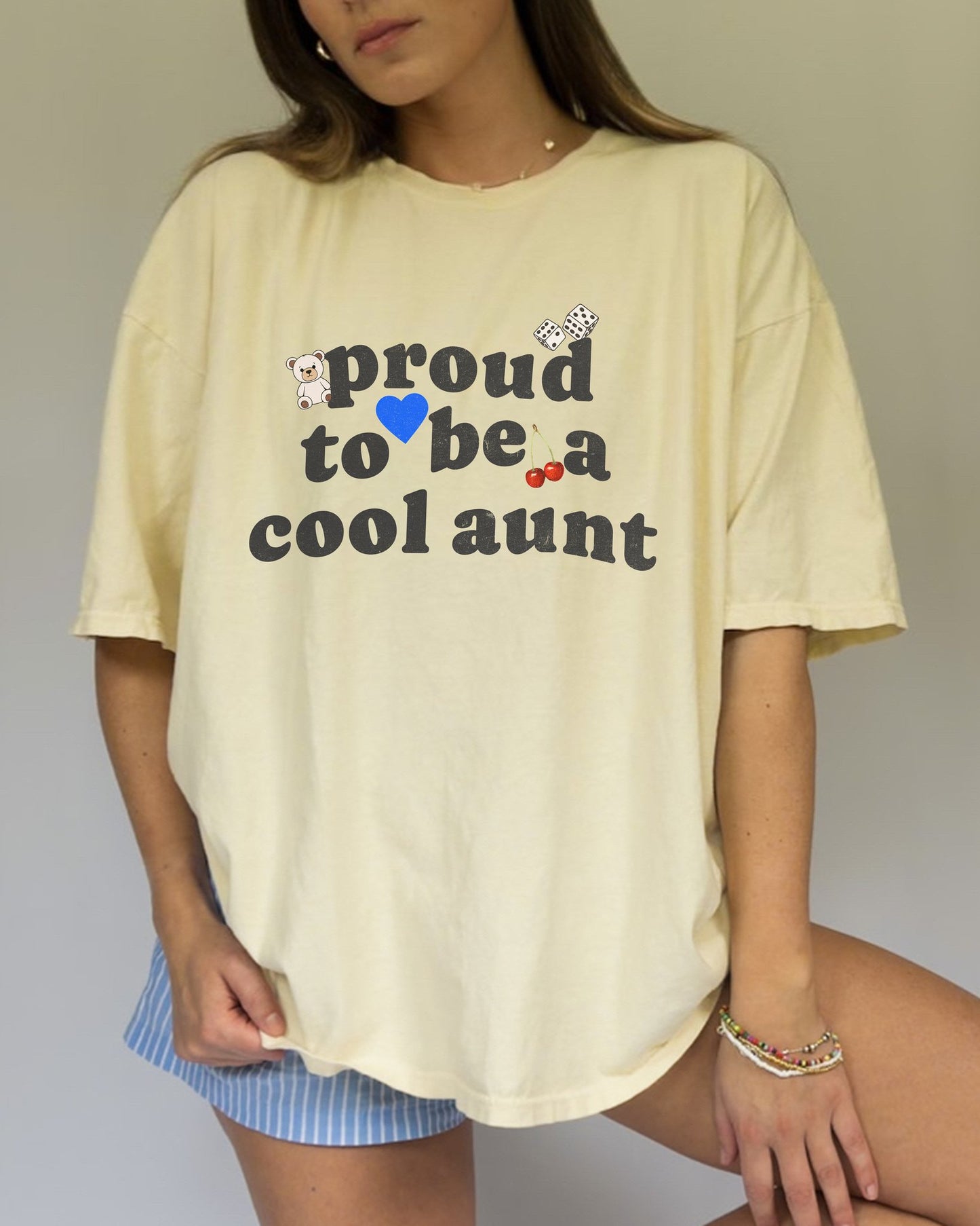 T-shirt with retro distressed text 'proud to be a cool aunt' decorated with teddy bear, blue heart, dice, and cherries