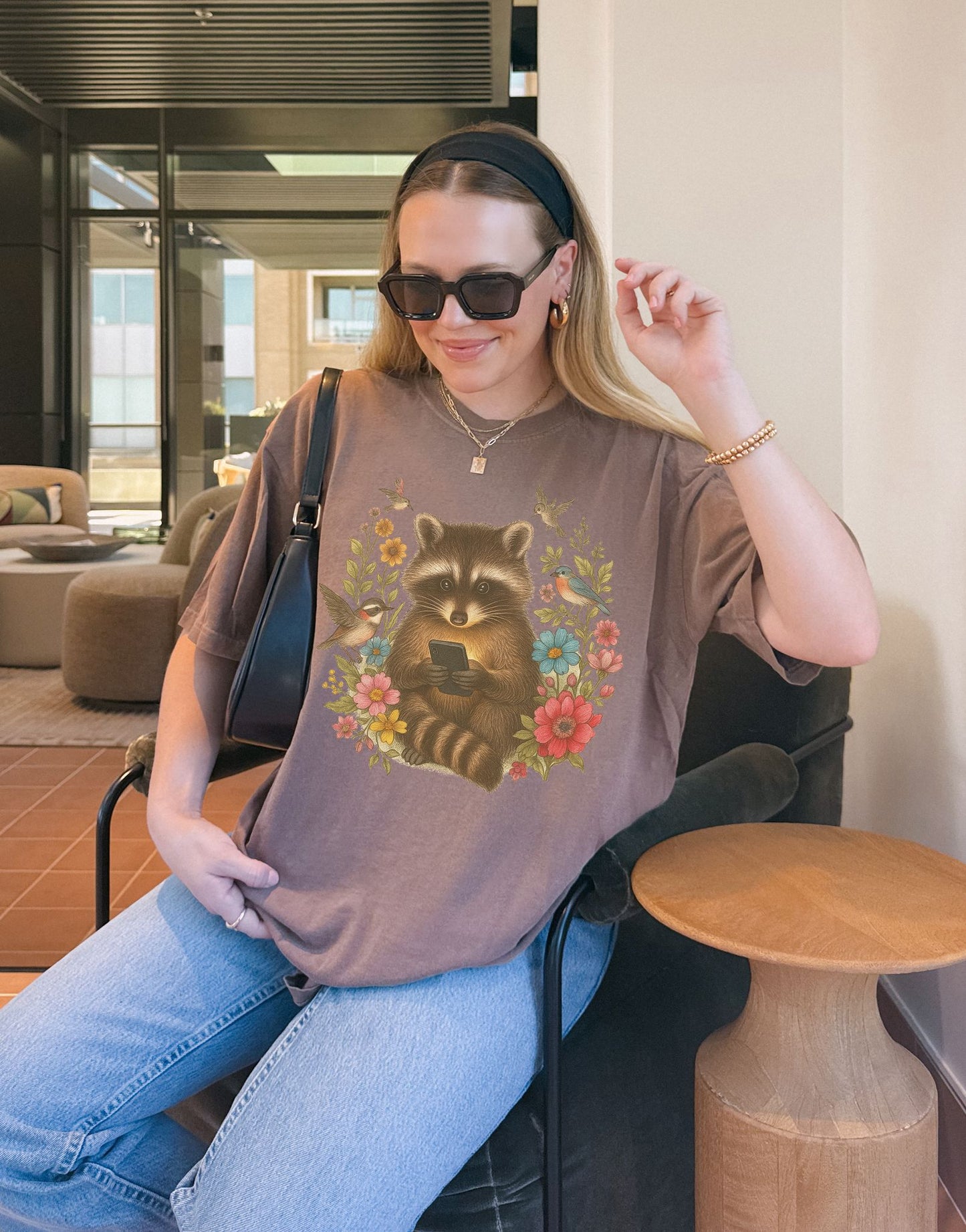 T-shirt design showing raccoon holding phone surrounded by colorful wildflowers and birds