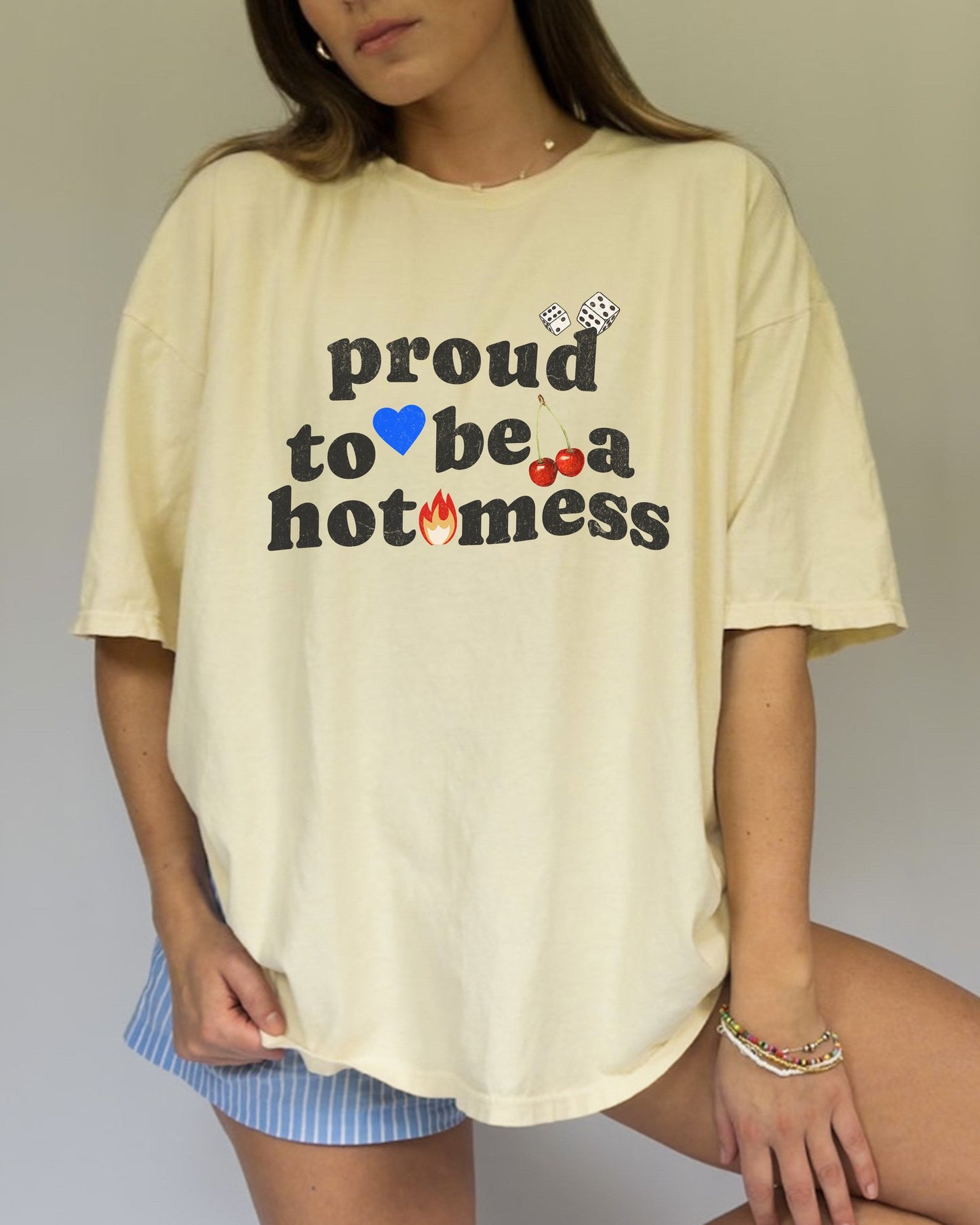 T-shirt with distressed black text reading 'proud to be a hot mess' decorated with dice, blue heart, cherries, and flame graphics