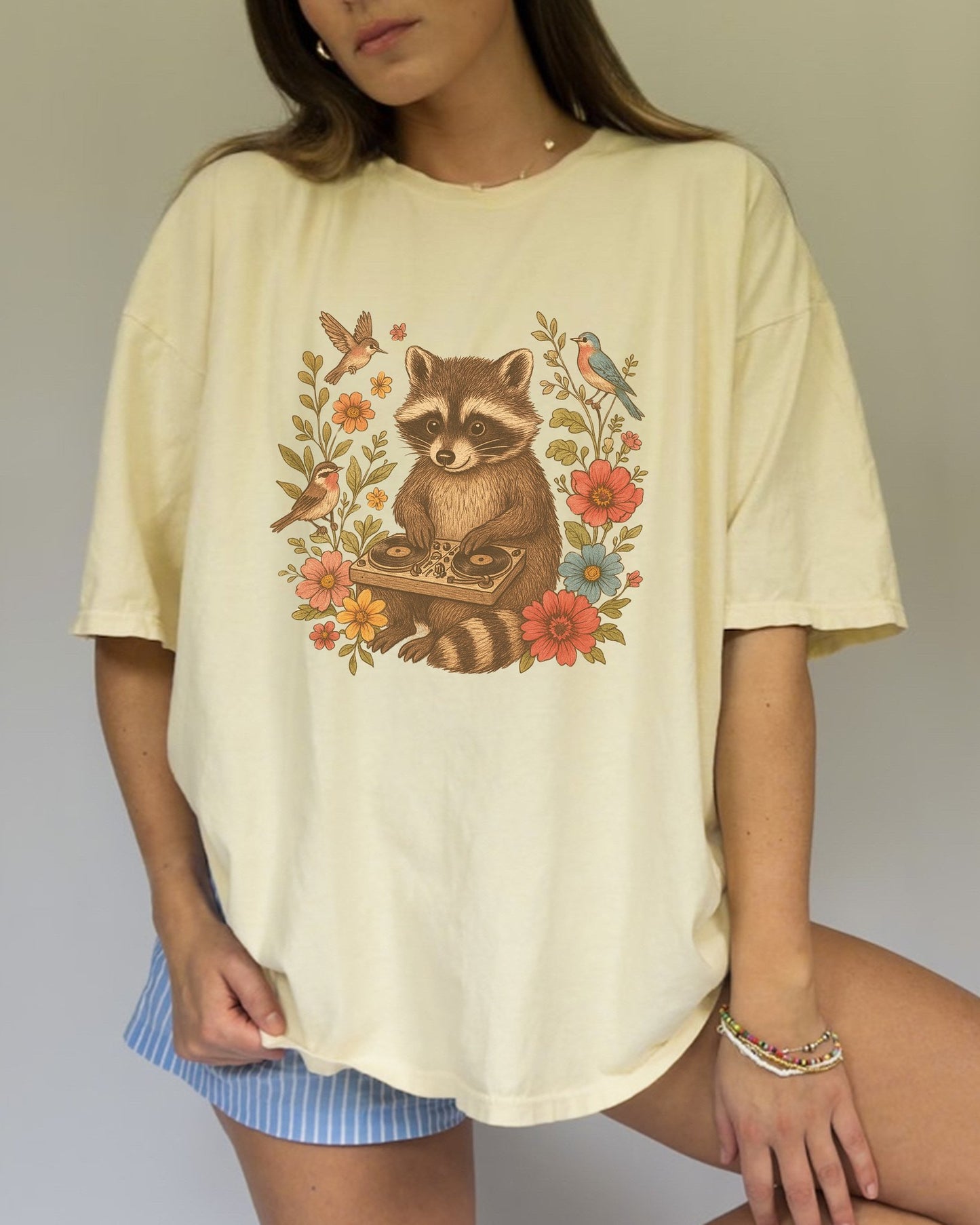 T-shirt with vintage raccoon DJ design surrounded by coral flowers, yellow blooms, and songbirds