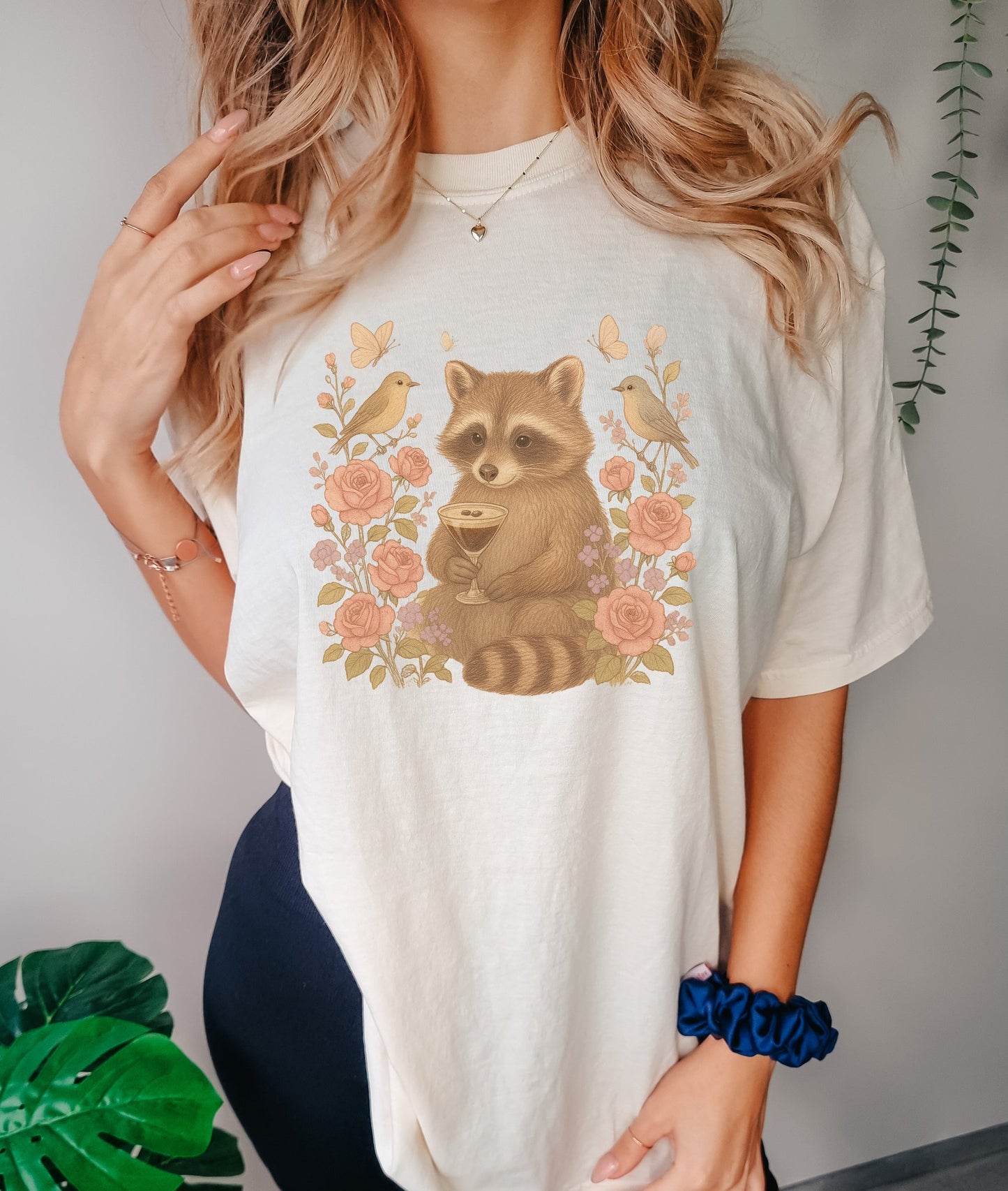 T-shirt with raccoon holding espresso martini glass surrounded by pink roses and birds