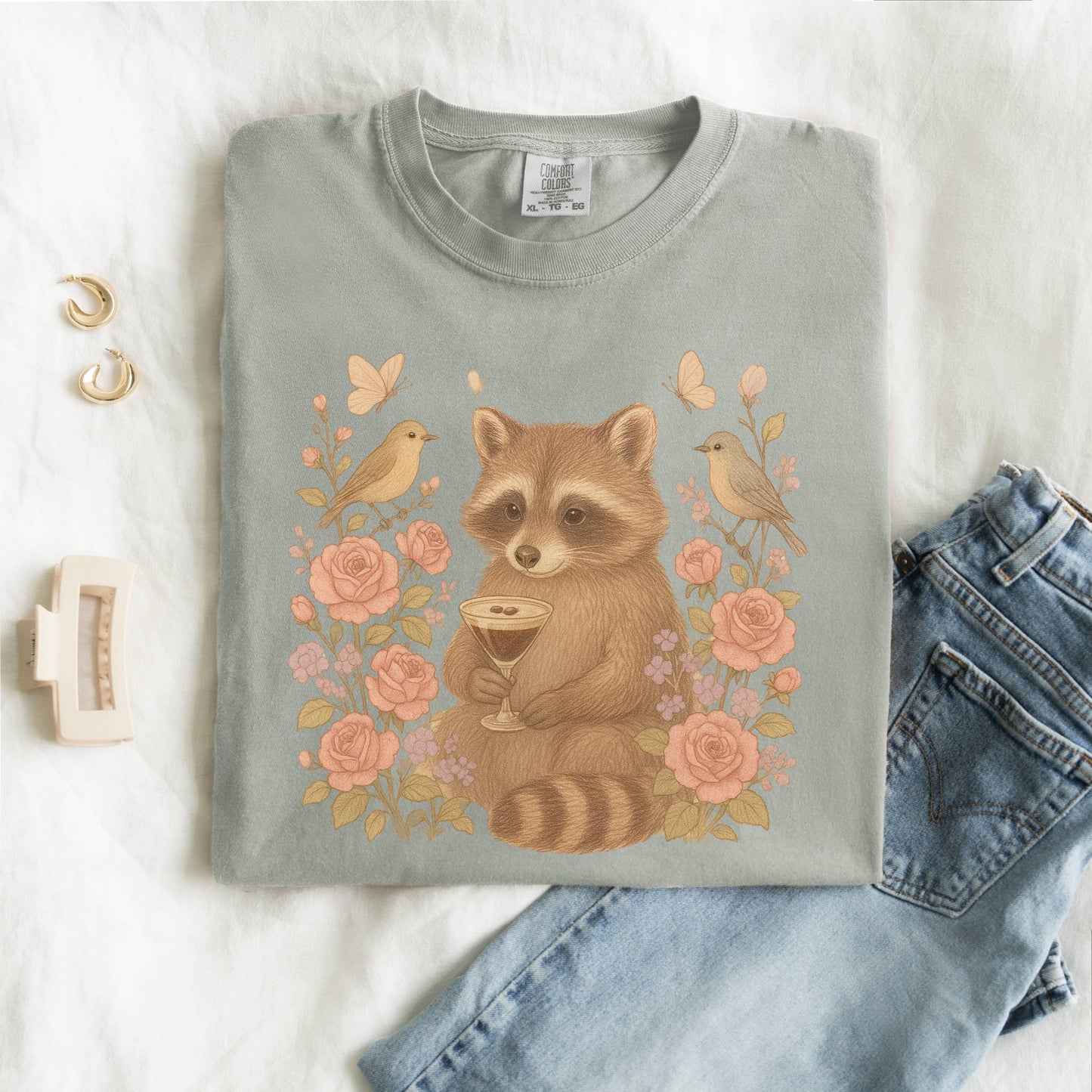 T-shirt with raccoon holding espresso martini glass surrounded by pink roses and birds