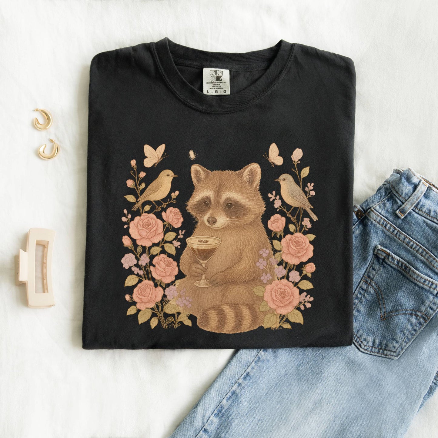 T-shirt with raccoon holding espresso martini glass surrounded by pink roses and birds