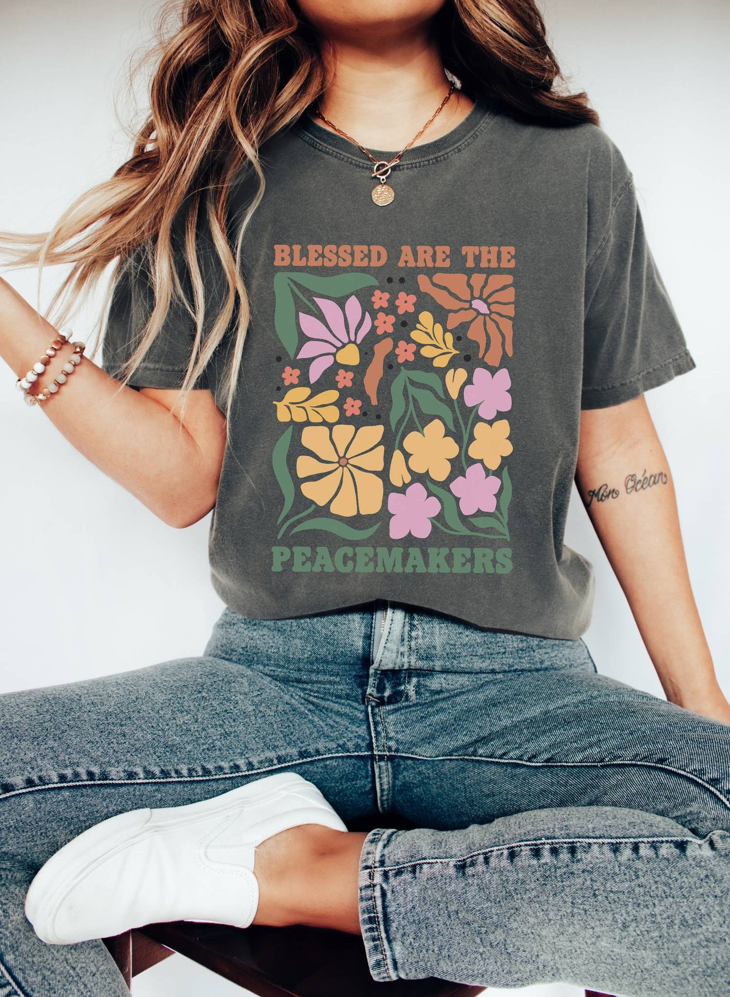 T-shirt with 'Blessed Are The Peacemakers' text surrounded by colorful floral design in pink, coral, yellow and green