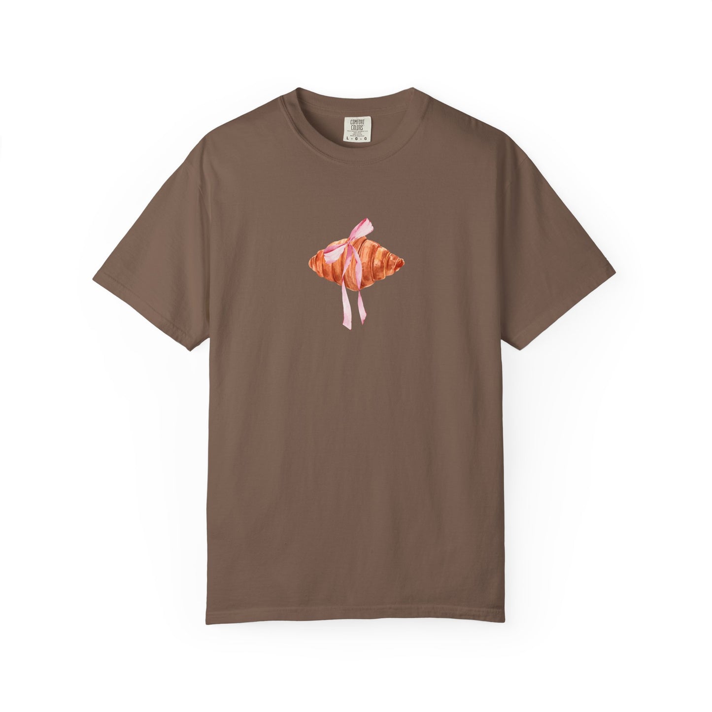 T-shirt with watercolor croissant design featuring golden brown pastry with pink ribbon bow