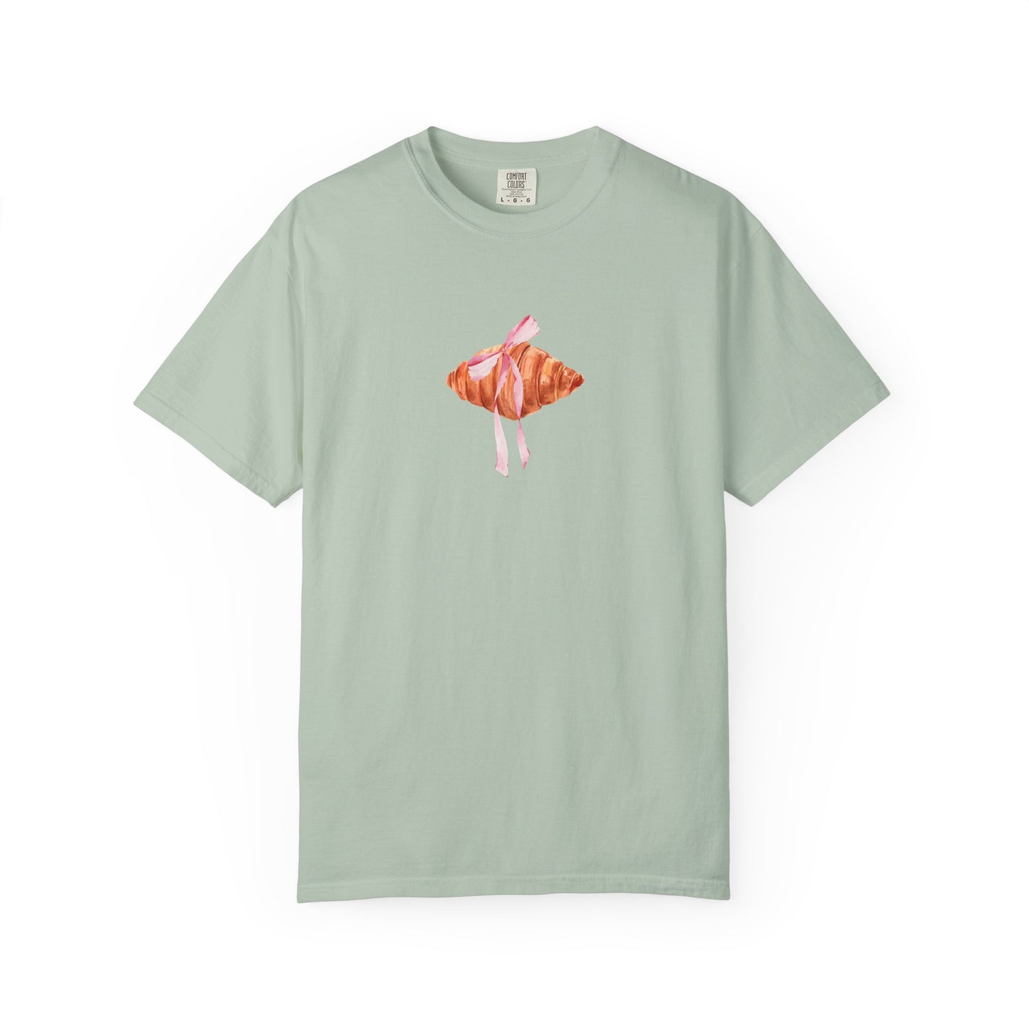 T-shirt with watercolor croissant design featuring golden brown pastry with pink ribbon bow
