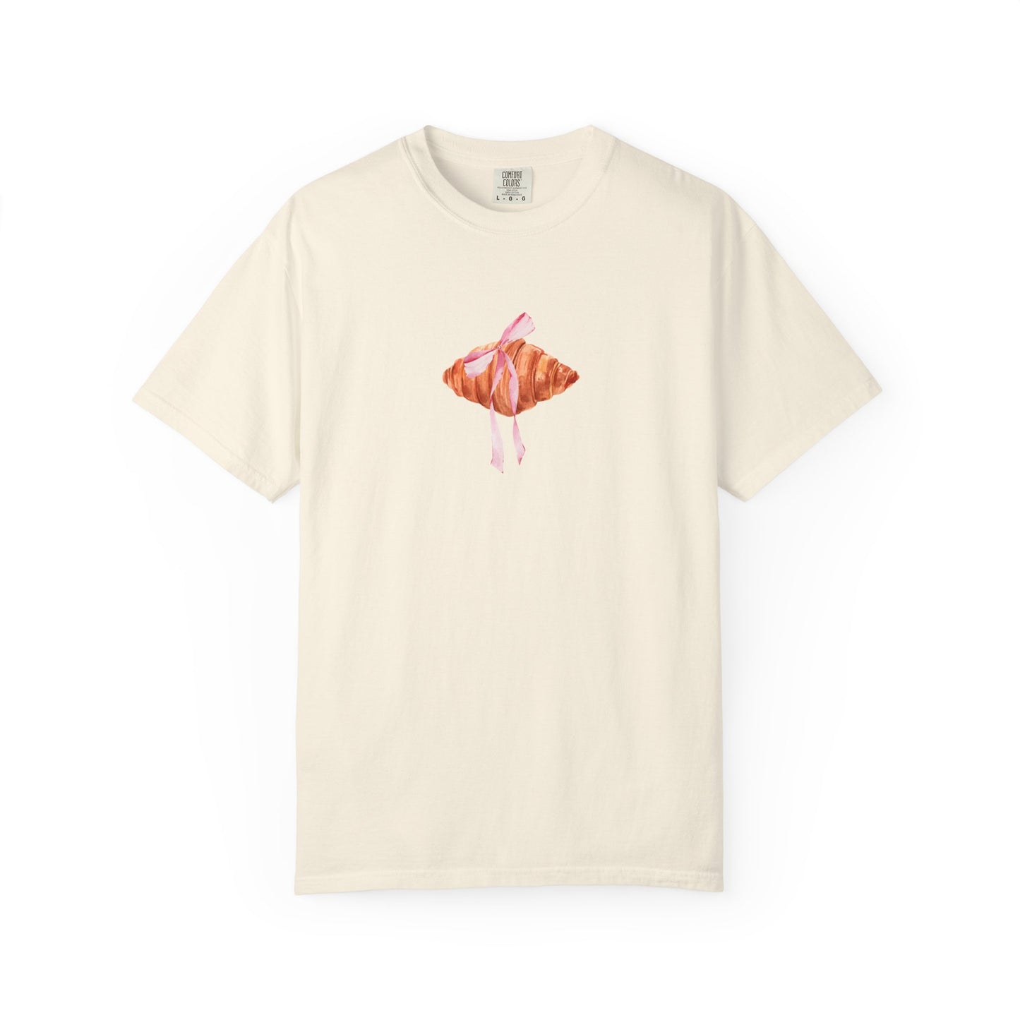T-shirt with watercolor croissant design featuring golden brown pastry with pink ribbon bow