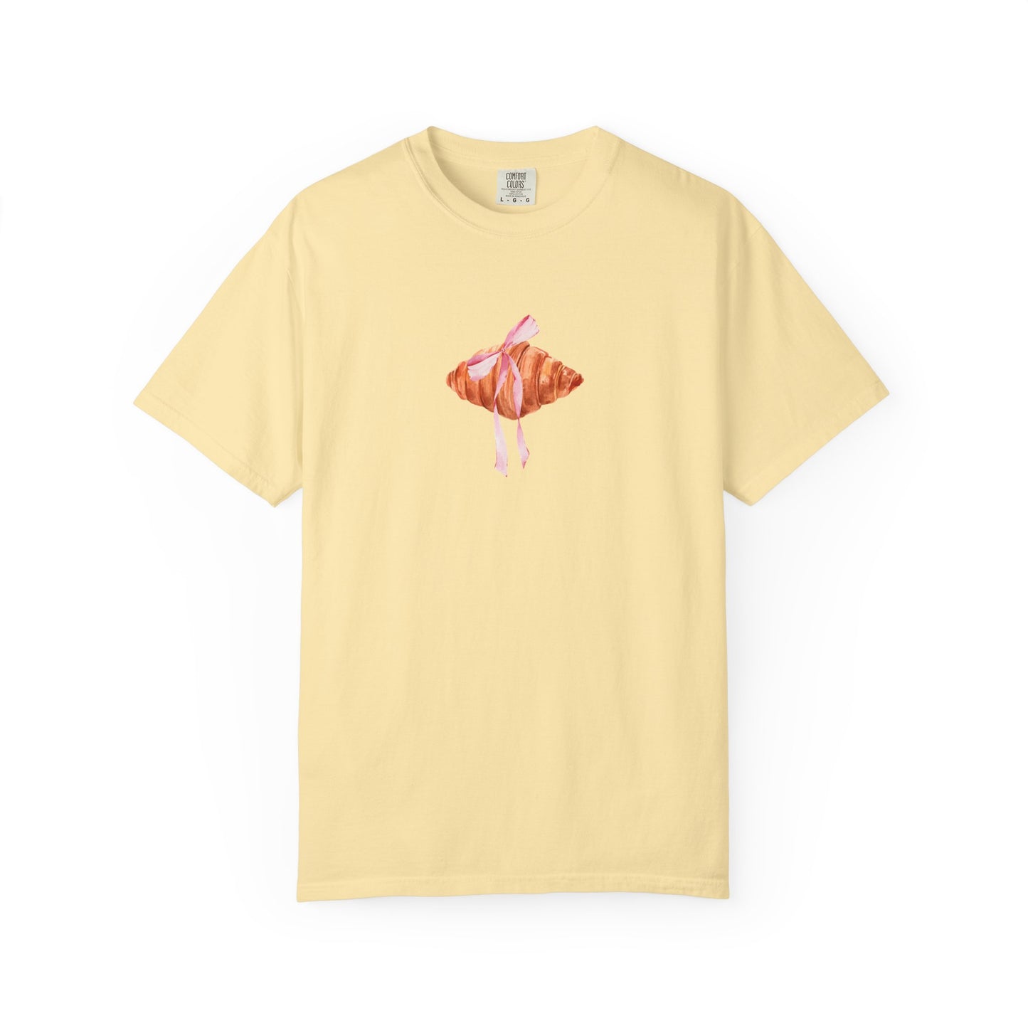 T-shirt with watercolor croissant design featuring golden brown pastry with pink ribbon bow