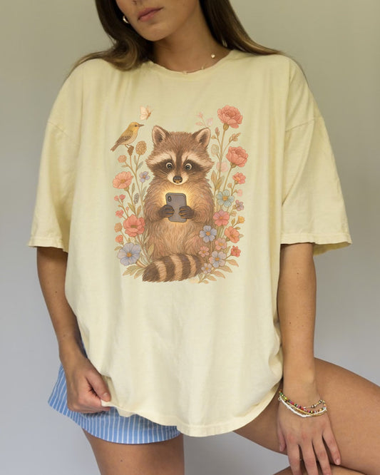 T-shirt with cute raccoon holding smartphone surrounded by coral and blue wildflowers