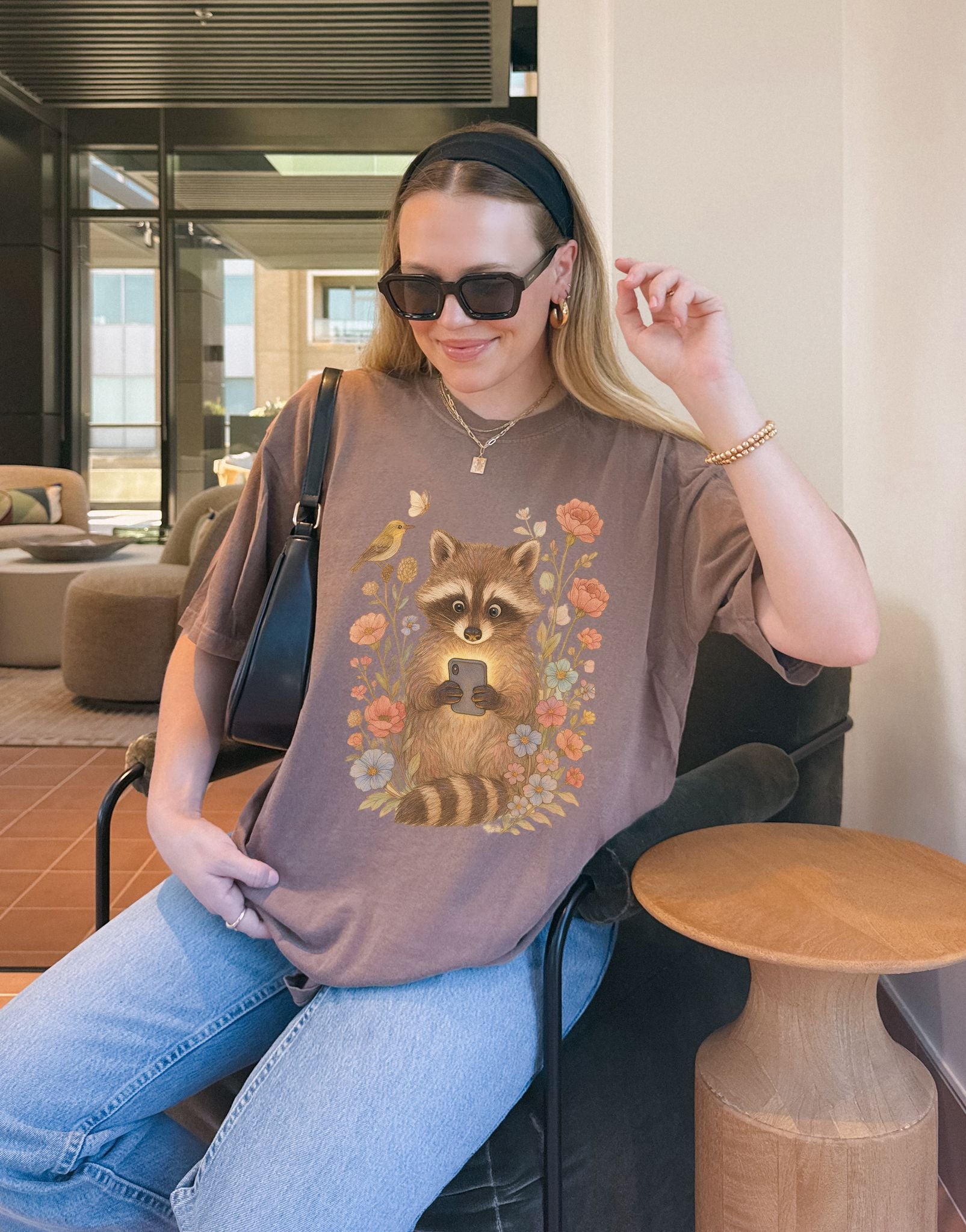 T-shirt with cute raccoon holding smartphone surrounded by coral and blue wildflowers