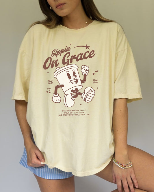 Christian t-shirt with cartoon coffee cup character and 'Sippin' On Grace' text in brown design