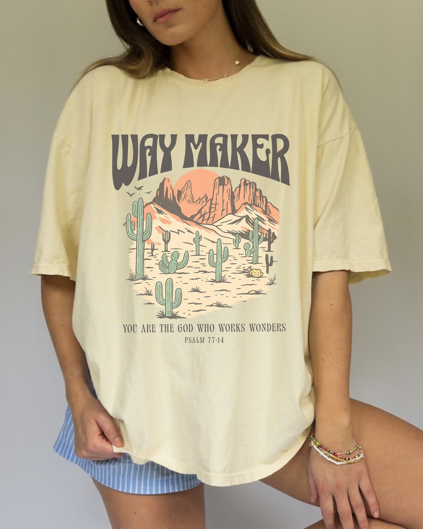 T-shirt with Way Maker text, desert landscape featuring cacti, mountains, and orange sunset with Psalm 77:14 verse
