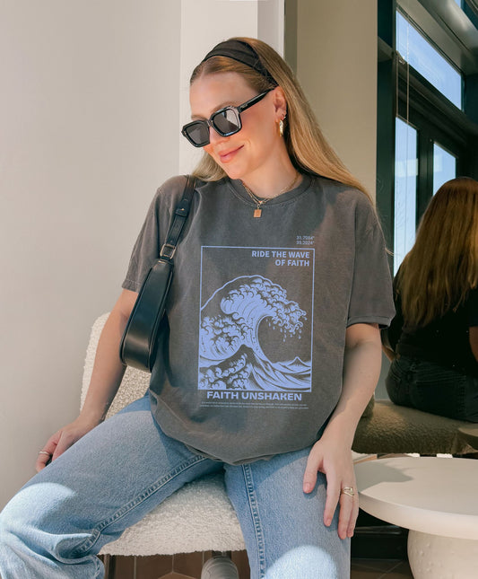 T-shirt with blue ocean wave design featuring 'Ride The Wave Of Faith' and 'Faith Unshaken' text