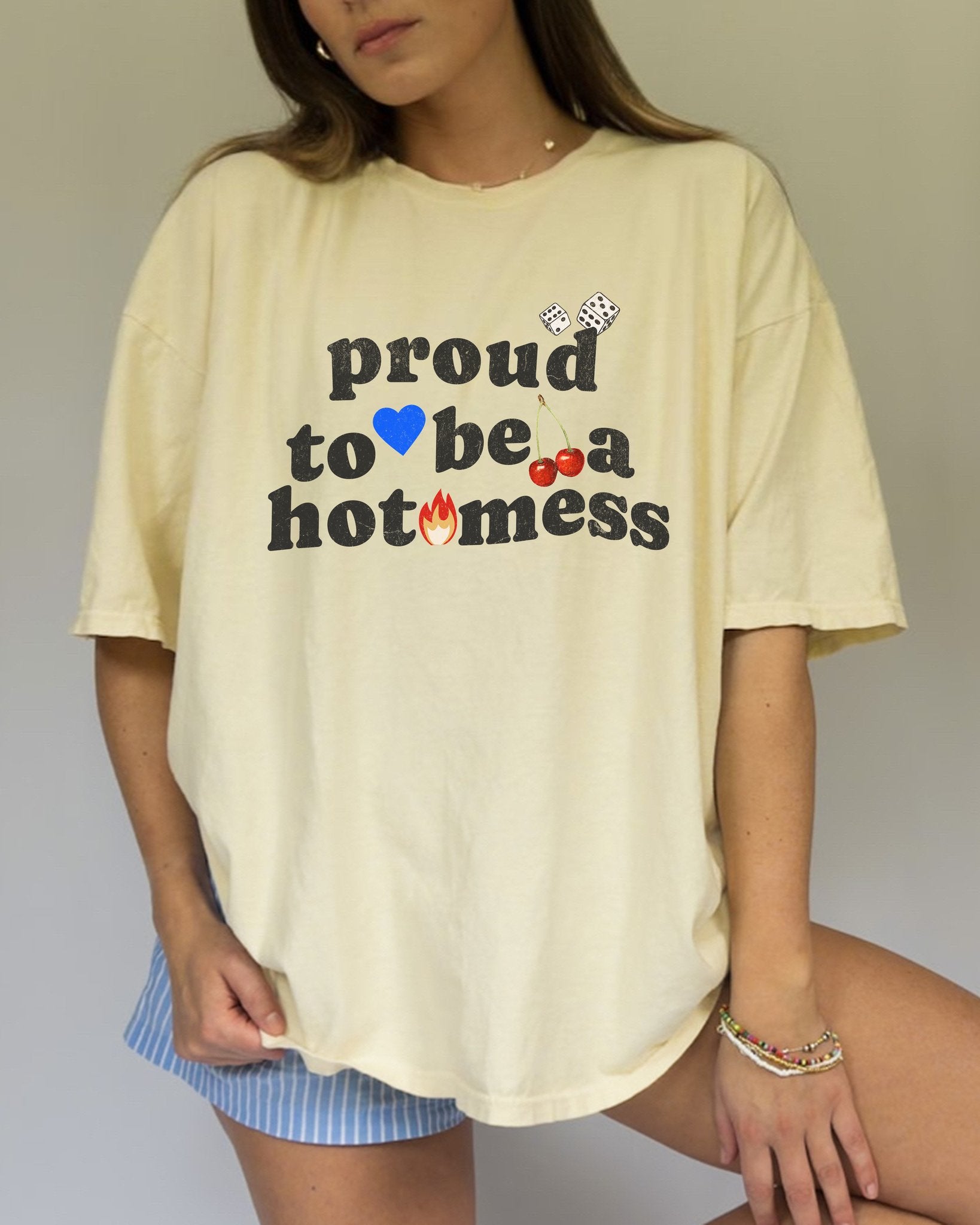 T-shirt with distressed black text reading 'proud to be a hot mess' decorated with dice, blue heart, cherries, and flame graphics