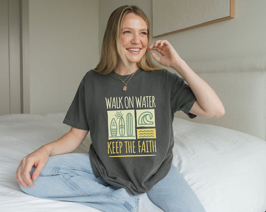 T-shirt with yellow Walk On Water Keep The Faith text, retro surfboard graphics and teal wave designs