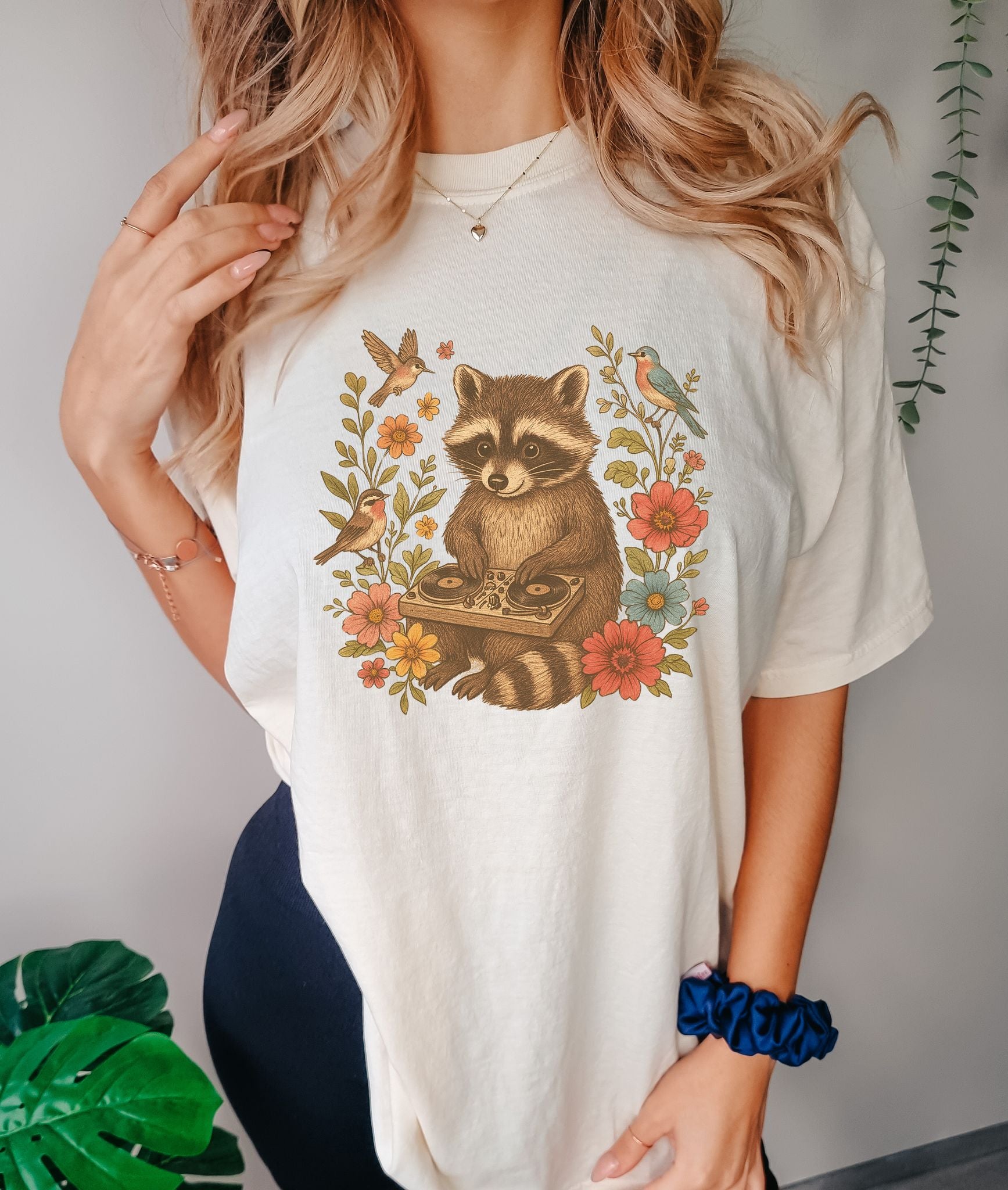 T-shirt with vintage raccoon DJ design surrounded by coral flowers, yellow blooms, and songbirds