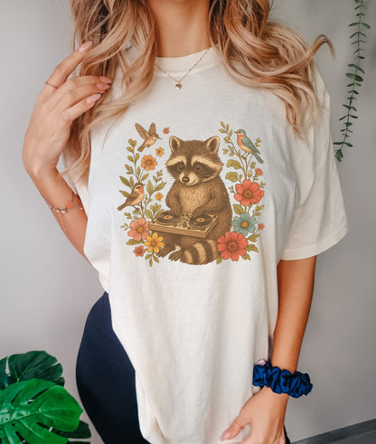 T-shirt with vintage raccoon DJ design surrounded by coral flowers, yellow blooms, and songbirds