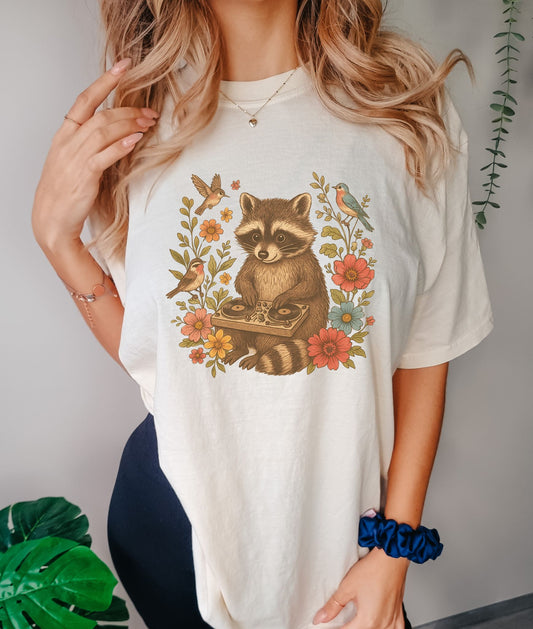 T-shirt with vintage raccoon DJ design surrounded by coral flowers, yellow blooms, and songbirds