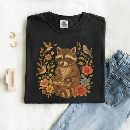 T-shirt with vintage raccoon DJ design surrounded by coral flowers, yellow blooms, and songbirds