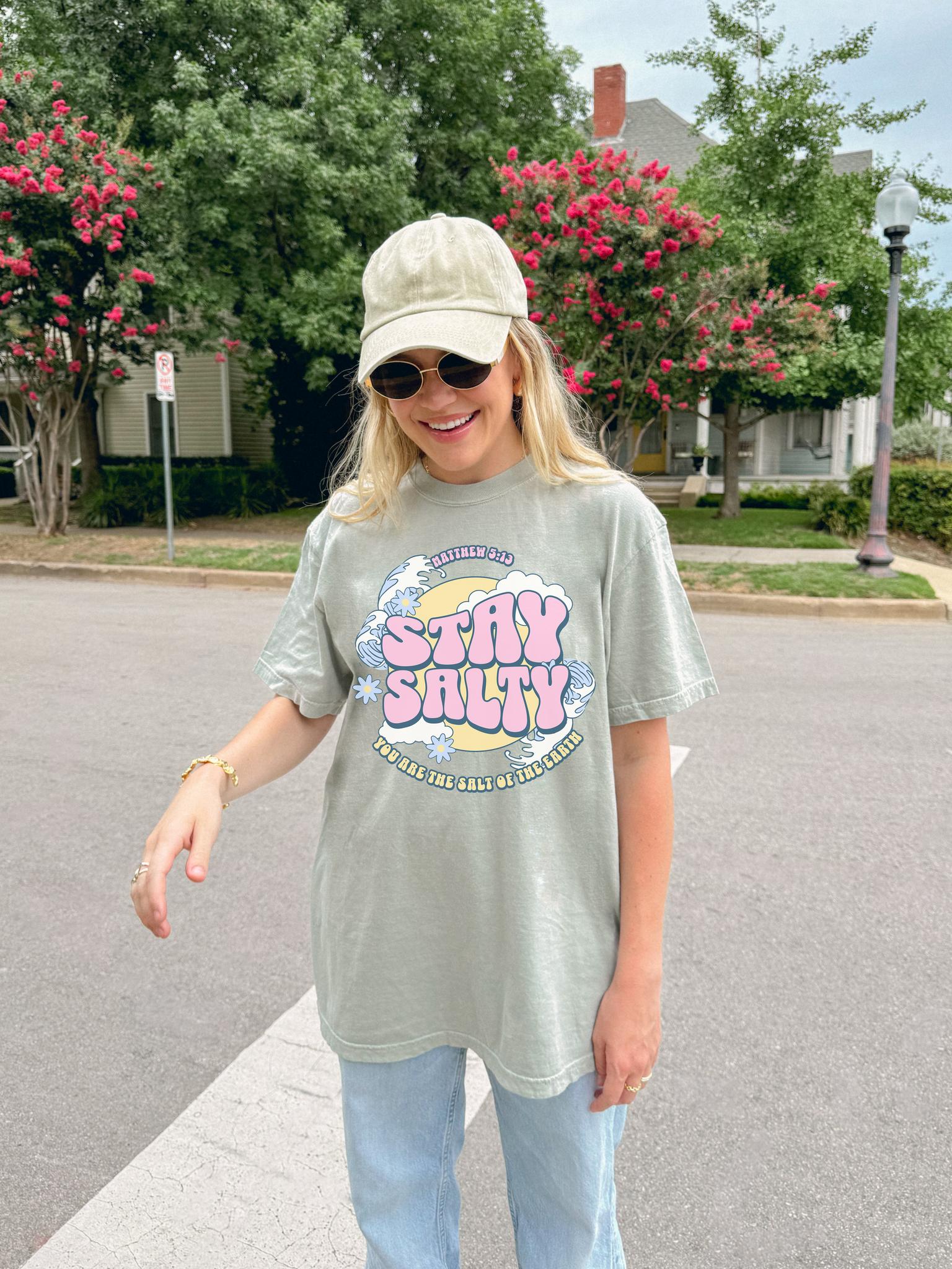 Christian t-shirt with pink 'Stay Salty' text, Matthew 5:13 verse, ocean waves and daisy flowers