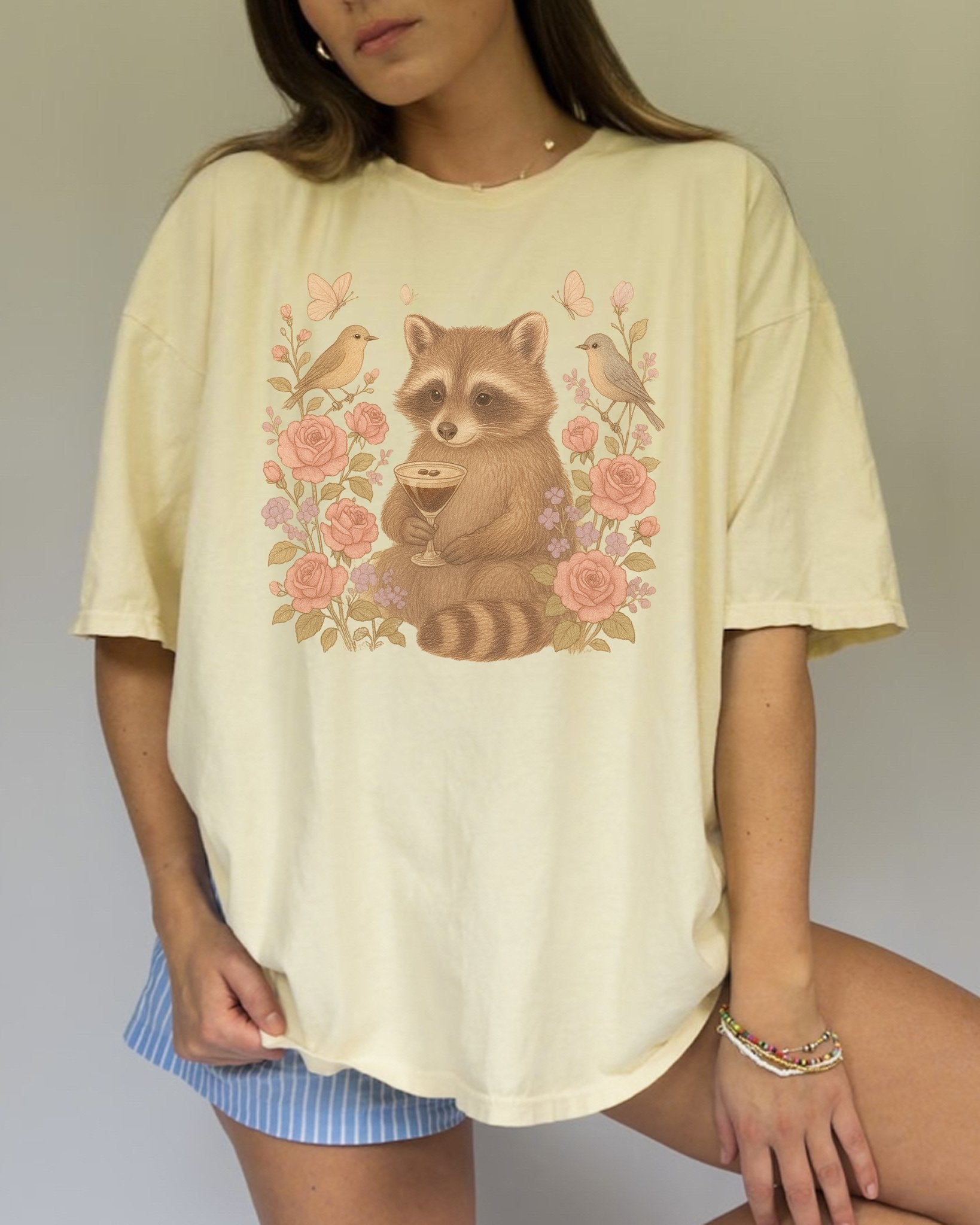 T-shirt with raccoon holding espresso martini glass surrounded by pink roses and birds