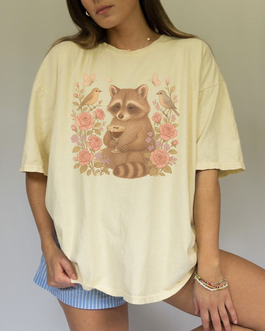 T-shirt with raccoon holding espresso martini glass surrounded by pink roses and birds