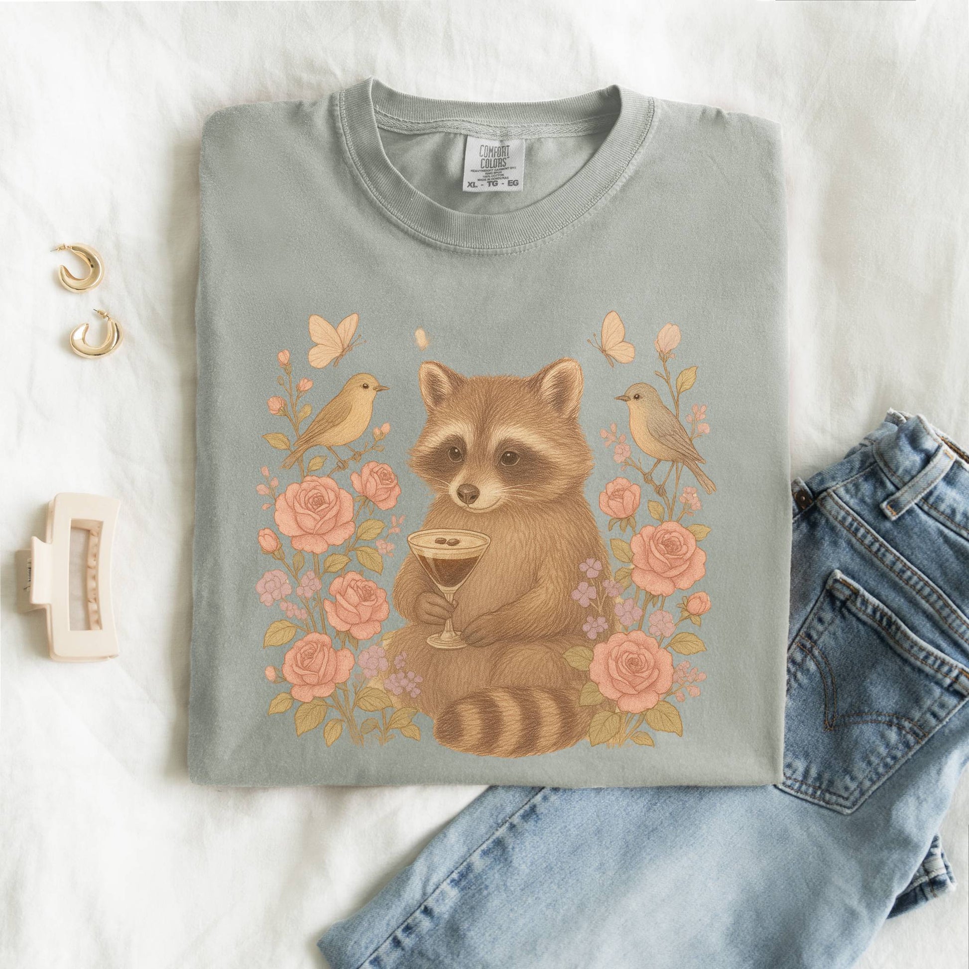 T-shirt with raccoon holding espresso martini glass surrounded by pink roses and birds