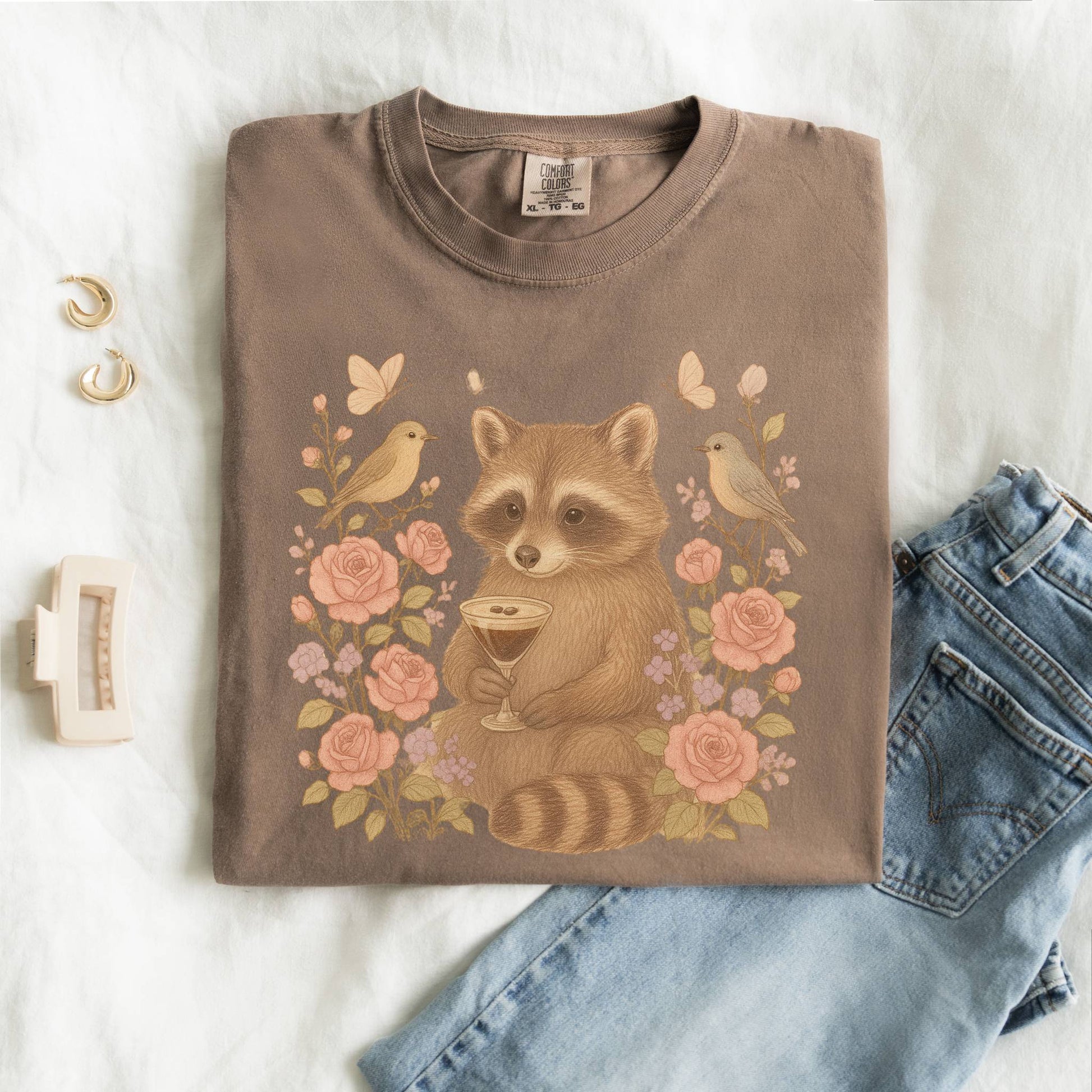T-shirt with raccoon holding espresso martini glass surrounded by pink roses and birds