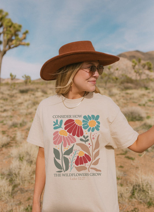T-shirt with Luke 12:27 Bible verse and colorful wildflowers in red, pink, teal, and brown tones