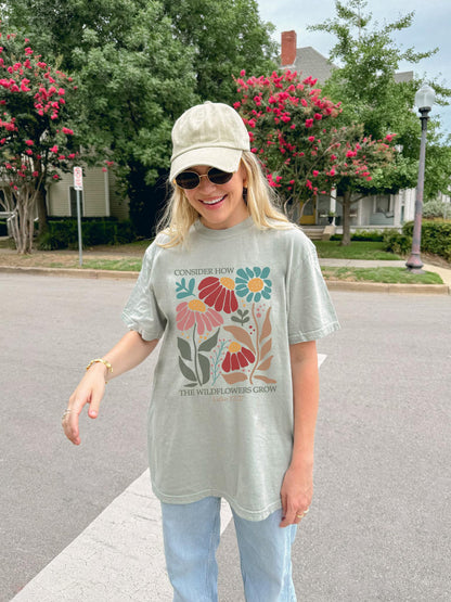 T-shirt with Luke 12:27 Bible verse and colorful wildflowers in red, pink, teal, and brown tones