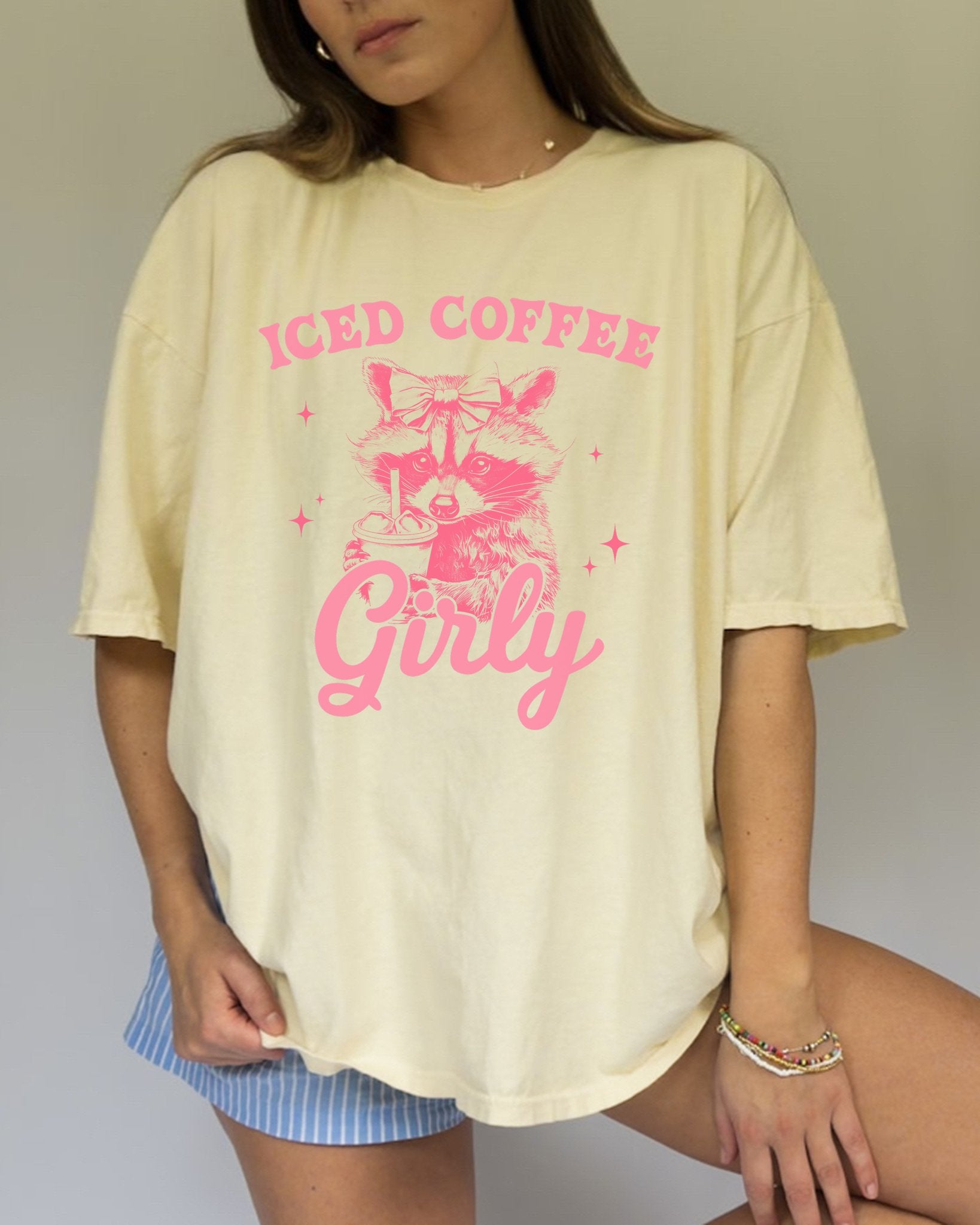 T-shirt with pink raccoon wearing bow holding iced coffee cup with 'Iced Coffee Girl' text and stars