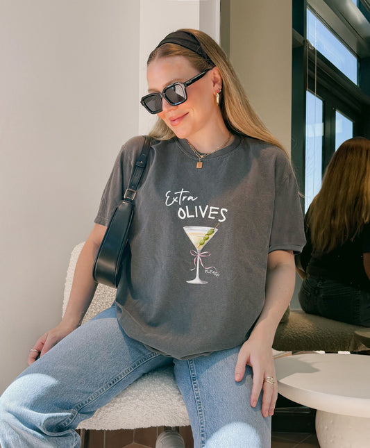 T-shirt design with martini glass, green olives, and pink bow saying Extra Olives Please