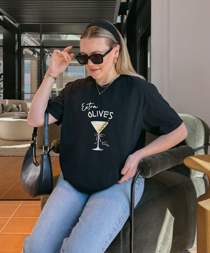 T-shirt design with martini glass, green olives, and pink bow saying Extra Olives Please