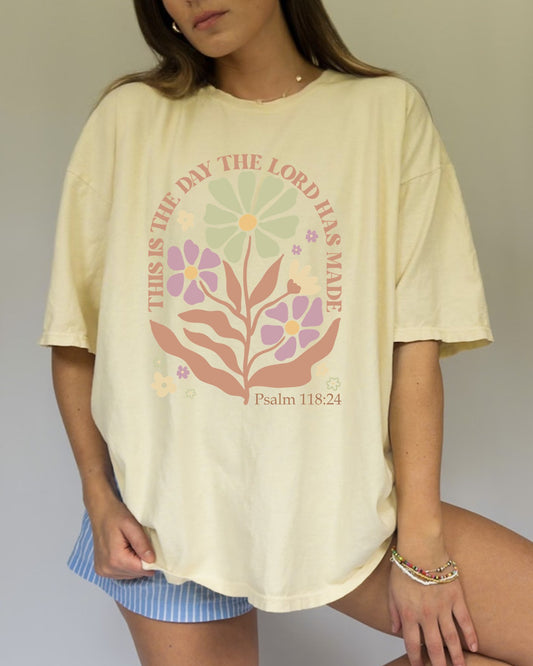 T-shirt with 'This is the Day' text, Psalm 118:24 verse, and floral design with protective hands in sage green, pink, and terracotta colors