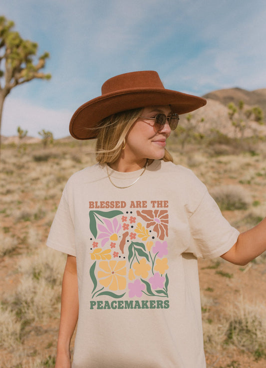T-shirt with 'Blessed Are The Peacemakers' text surrounded by colorful floral design in pink, coral, yellow and green